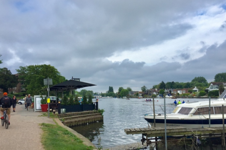 The riverside in Elmbridge with a boat in the foreground and a cyclist on the path.