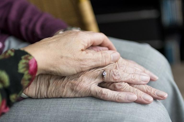A person holding the hand of an elderly person