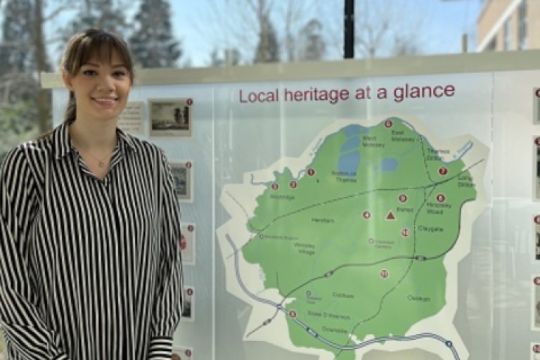Amy Swainston smiling and standing in front of a map of Elmbridge