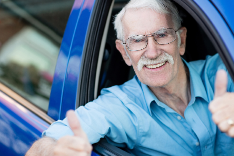 A man in a blue car with his thumbs up