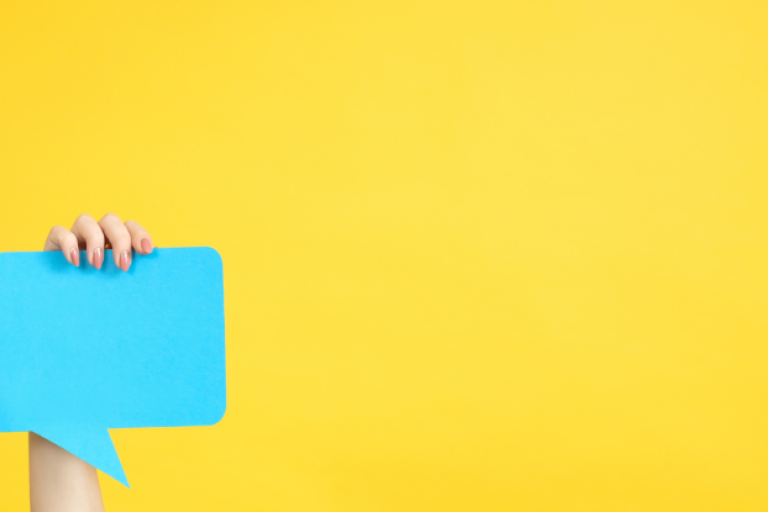 person holding up a blue speech bubble against a yellow background to represent asking for your views