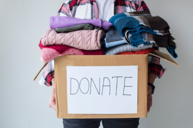 An image showing a person holding a box filled with clothes. On the front of the box, is a big 'donate' label. 