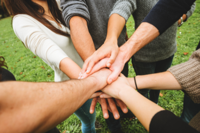 An image of a group of people showing unity by forming a circle and putting their hands on top of each other.
