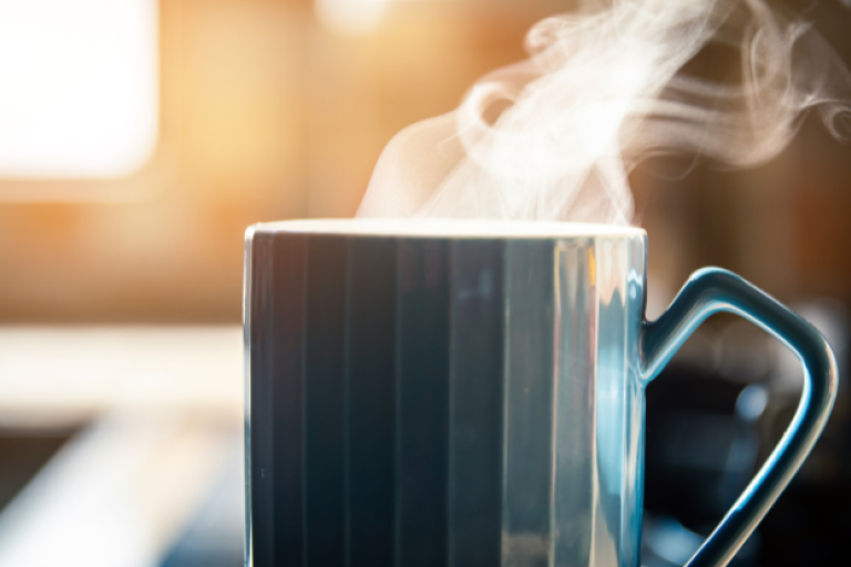 Mug with steam flowing out the top on a kitchen side