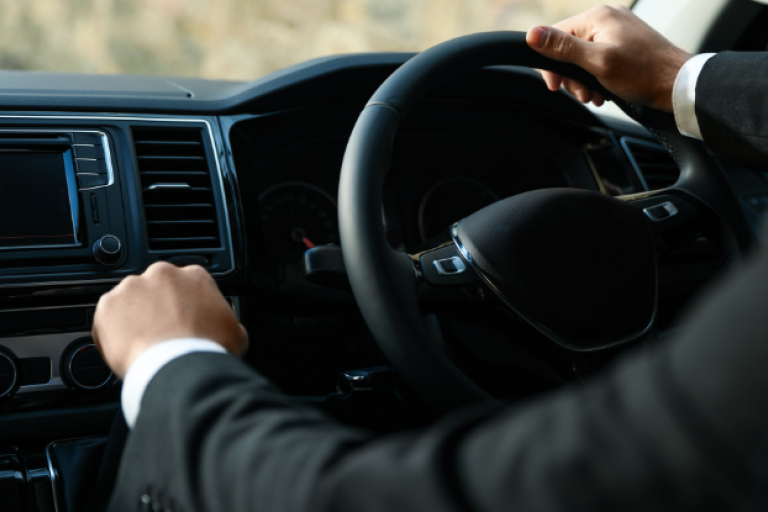 Driver in a suit with hands on a black steering wheel