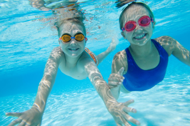 A boy and girl swimming under water with swim goggles on and smiling