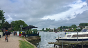 The riverside in Elmbridge with a boat in the foreground and a cyclist on the path.