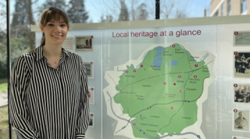 Amy Swainston smiling and standing in front of a map of Elmbridge