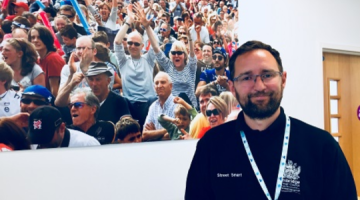 Martin Kearton smiling in front of an image on the wall of a group of people