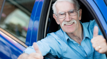 A man in a blue car with his thumbs up