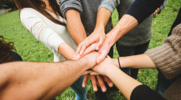 An image of a group of people showing unity by forming a circle and putting their hands on top of each other.