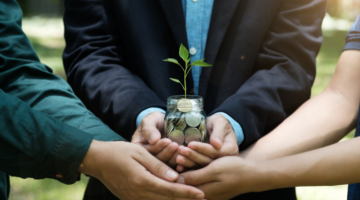 Hands of three people holding a glass jar of money with a plant growing within it