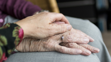 Woman's hand placed on top of an elderly woman's hands rested on her lap