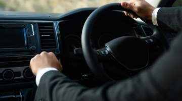 Driver in a suit with hands on a black steering wheel