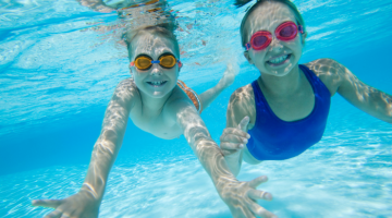 A boy and girl swimming under water with swim goggles on and smiling